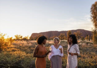 three women drinking champagne in front of uluru
