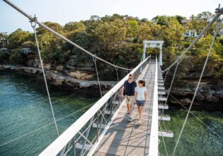 A couple cross the suspension bridge at Parsley Bay while walking the Bondi to Manly coastal walk