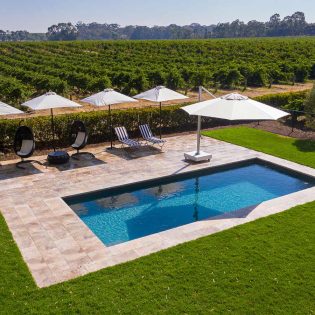 an outdoor pool with umbrellas and sun loungers surrounded by an expansive vineyard in Le Mas, Barossa Valley
