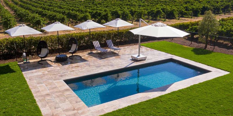 an outdoor pool with umbrellas and sun loungers surrounded by an expansive vineyard in Le Mas, Barossa Valley