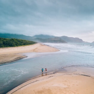 Two people crossing a beach along the Thorsborne Trail