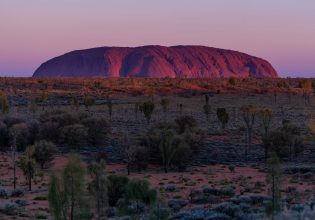 The sun sets over one of the great natural wonders of the world, Uluru towers above the surrounding landscape. (Image: Tourism NT/Che Chorley)